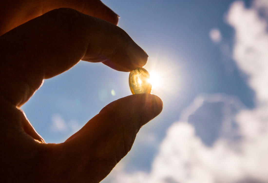 Hand holding a Vitamin D capsule against sunlight, symbolising the importance of Vitamin D for health and stress management.