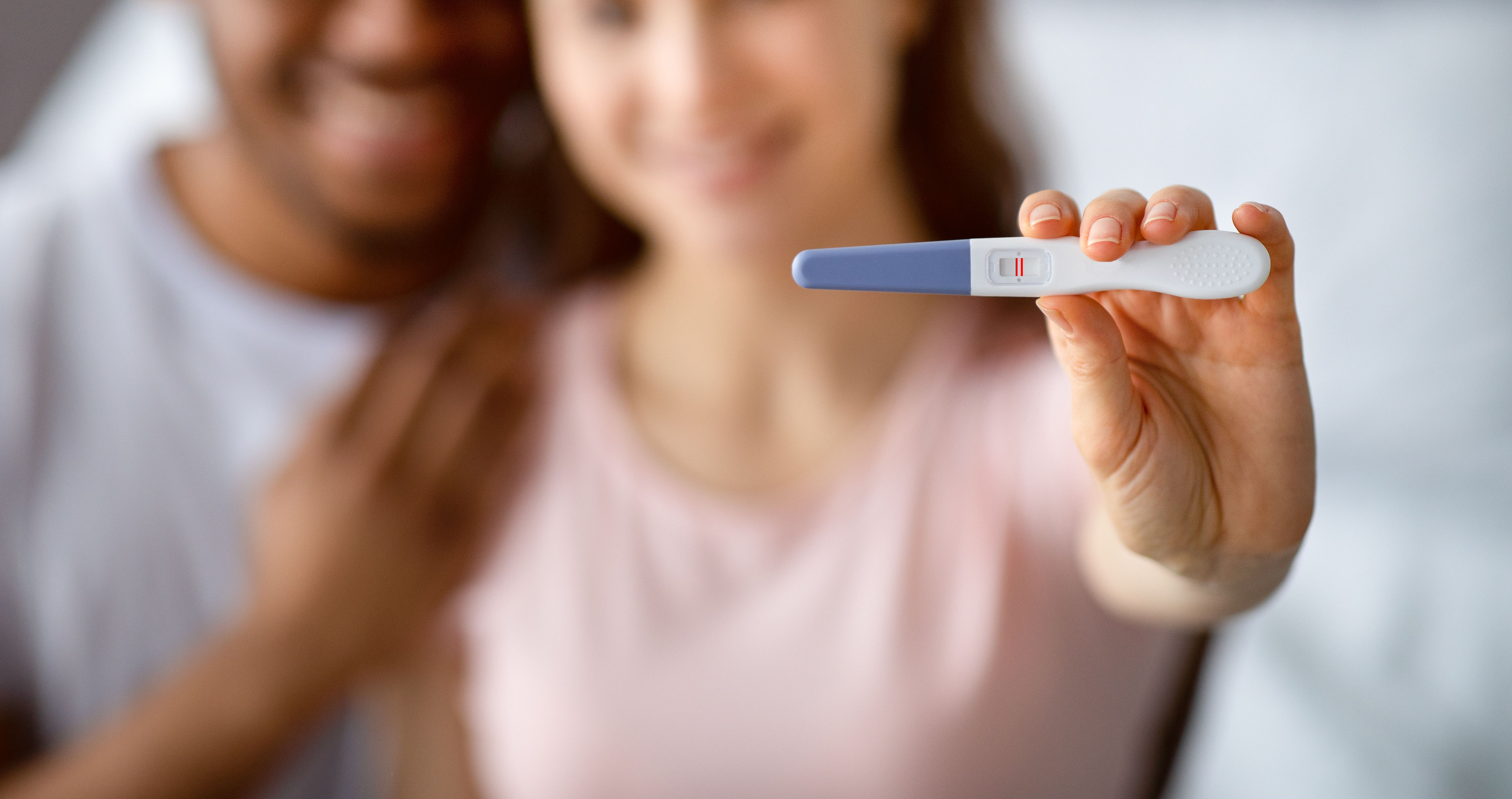 Woman holding a positive pregnancy test while standing with partner, representing early pregnancy detection using home testing kits.