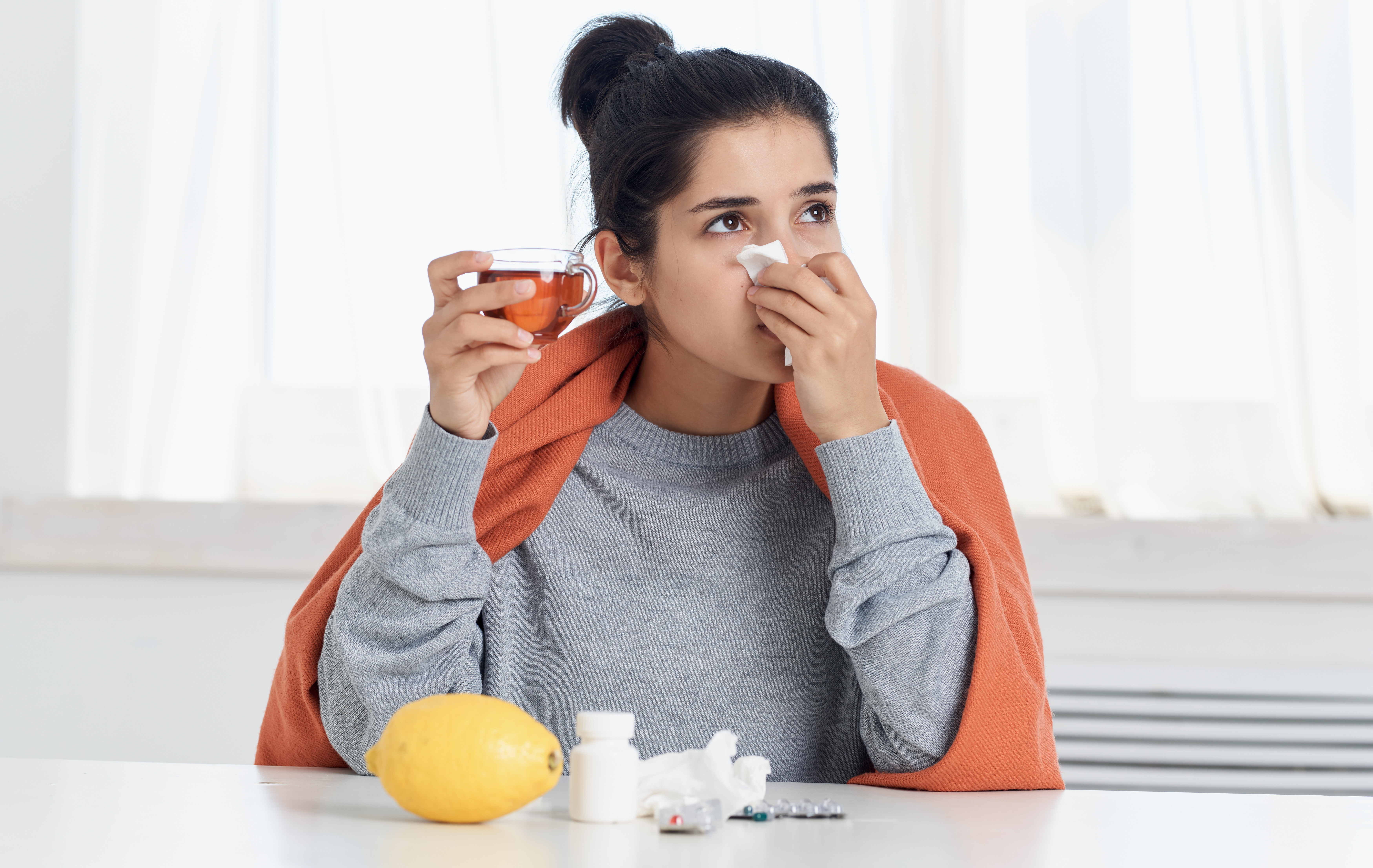 Woman with cold symptoms holding hot tea during winter health check at home.